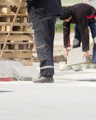 Construction worker in safety clothes cleaning building site after installing flagstones in sand